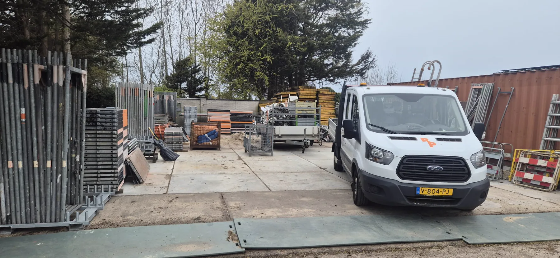 Pakvis-terrein met steigermateriaal, aanhanger en bedrijfsbus